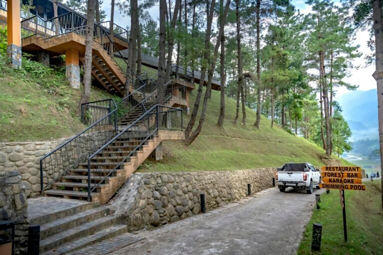 A mountain resort driveway surrounded by lush forest and distant hills.