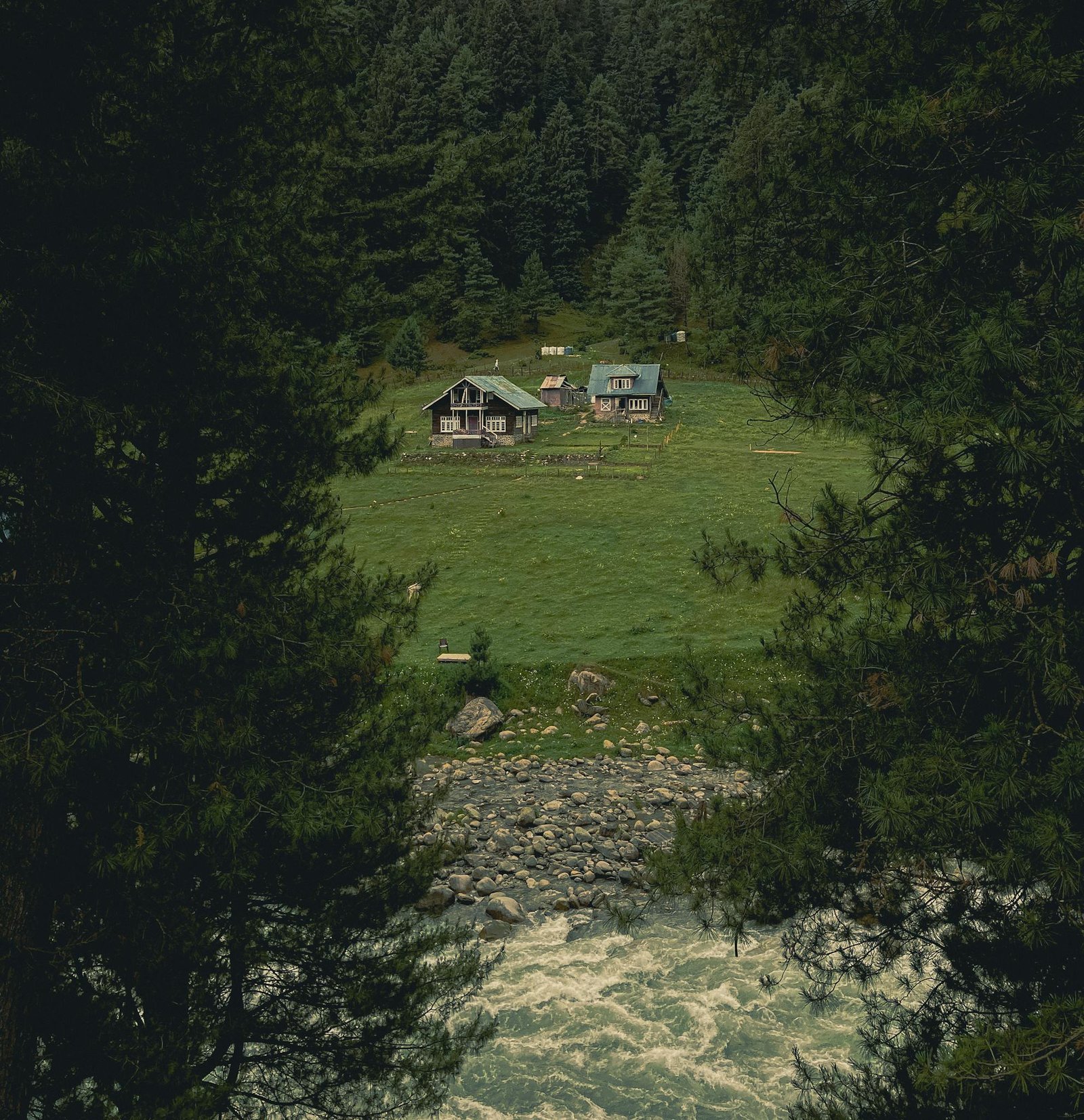 A picturesque landscape with forest cottages nestled between lush greenery and a flowing river.