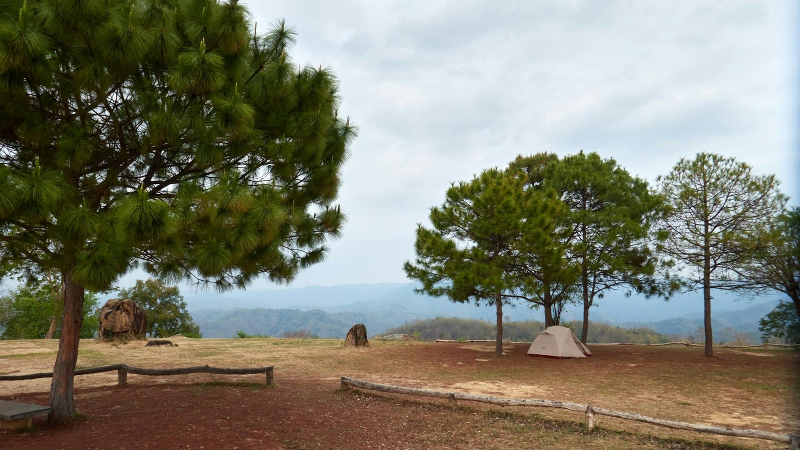 Peaceful highland camping scene in Thailand with a tent, trees, and a scenic mountain view.